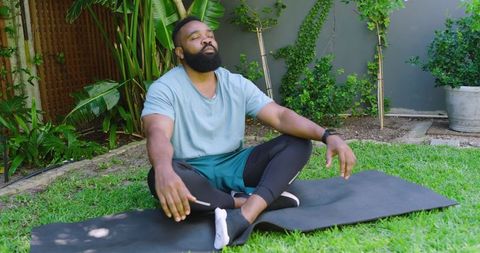 Man Meditating Outdoors on Yoga Mat in Lush Garden Setting