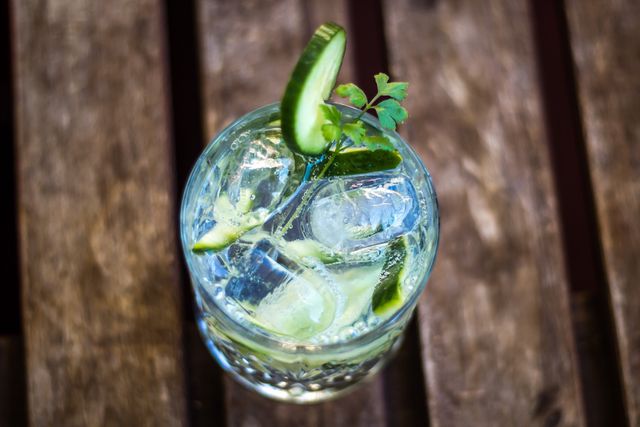 High-angle view of a refreshing gin and tonic with cucumber garnish and ice cubes in a clear glass. Ideal for promoting bars, summer refreshments, drink recipes, and evening social settings.