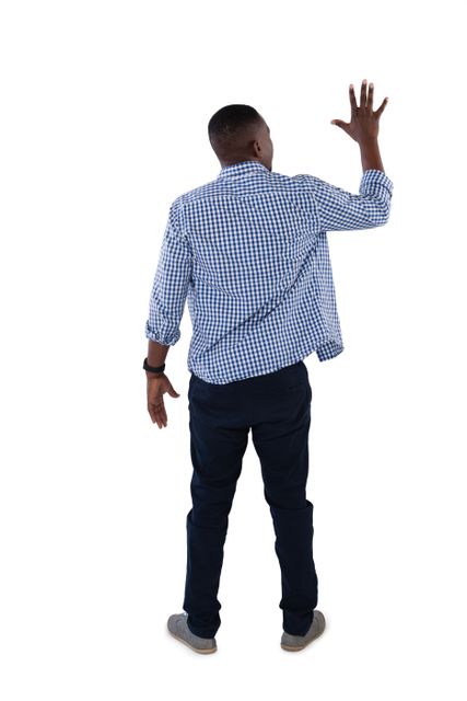 Man in casual clothing standing with his back to the camera, pretending to touch an invisible screen. Ideal for technology, virtual reality, and user interface concepts. Can be used in presentations, advertisements, and educational materials to illustrate interaction with digital interfaces.
