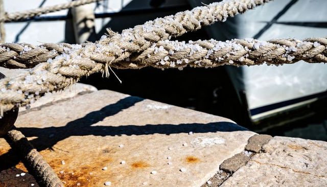 Weathered mooring ropes crossing stone quay with salt crystals and rust shadows