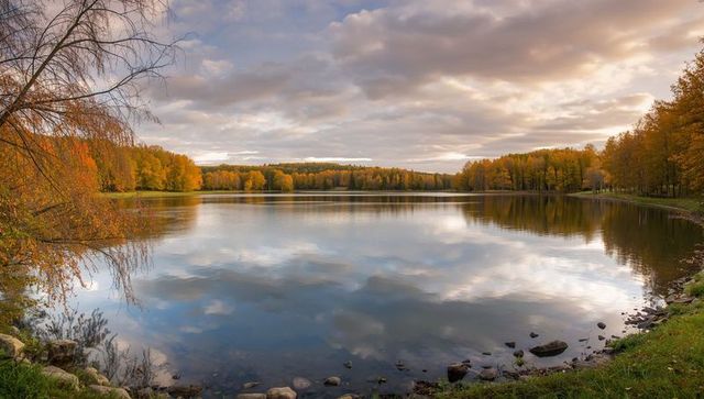 Serene lake reflecting cloudy sky with autumn foliage