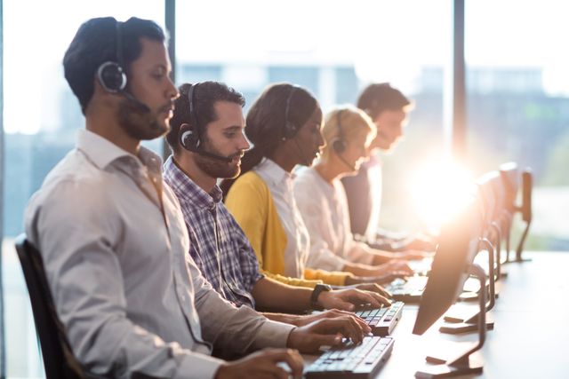 Customer service team working with headsets in a bright office. Ideal for illustrating teamwork, professional communication, business environments, and support staff operations. Useful for websites, brochures, and presentations related to customer service, office culture, and business services.
