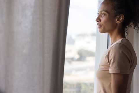Woman standing by window in soft natural light, contemplative urban interior lifestyle