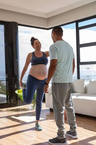 Pregnant Woman Stretching with Partner, Coastal Home Wellness