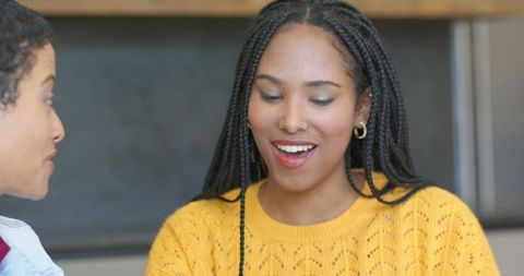African american friends chatting in modern kitchen wearing yellow sweater and braids