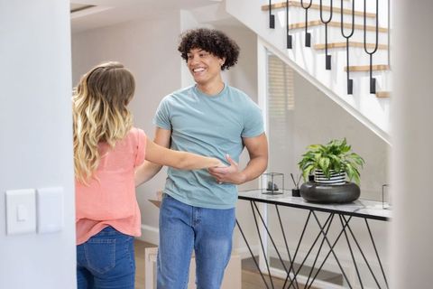 Young couple holding hands and smiling while unpacking boxes in modern minimalist entryway