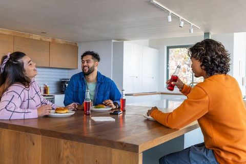 Friends laughing and eating burgers at wooden kitchen island with drinks, casual lifestyle