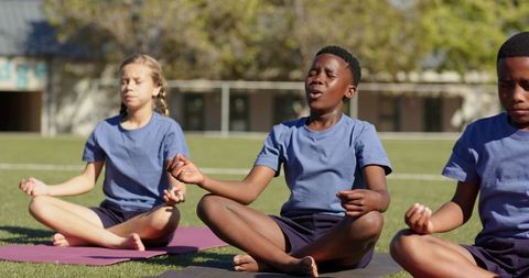 Multiracial teens practicing mindfulness on school field during outdoor yoga session