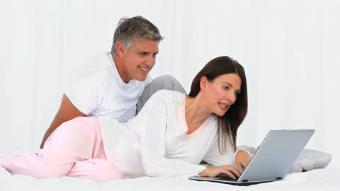 Couple Relaxing Together on Bed Using Laptop