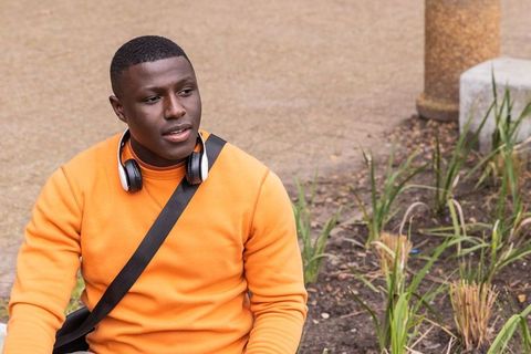 African american man sitting on urban walkway wearing orange sweatshirt and headphones