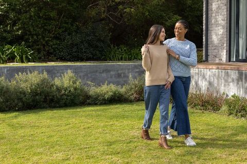 Multiracial women walking on lawn wearing sweaters and jeans sharing conversation