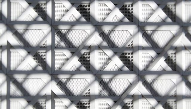 White perforated metal grid casting diagonal lattice shadows geometric facade pattern