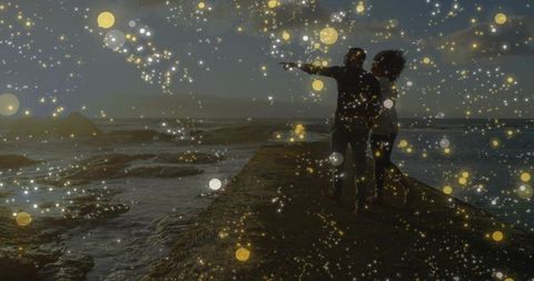 Silhouetted couple embracing on jetty at dusk with golden bokeh lights