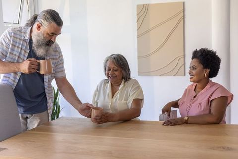 Multigenerational diverse family sharing coffee and conversation at sunlit wooden table