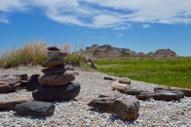 Stacked stones on rocky ground in a desert landscape with grassy area and cloudy sky. Useful for concepts of balance, mindfulness, and nature. Ideal for travel blogs, outdoor activity promotions, and nature preservation awareness.