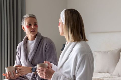 Mature women relaxing with under-eye patches sharing morning coffee in cozy bedroom