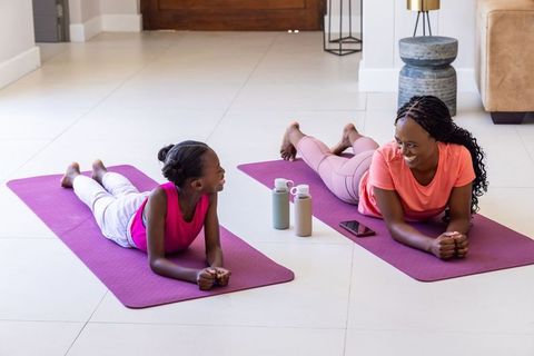 African mother and daughter stretching on yoga mats at home, sharing joyful bonding