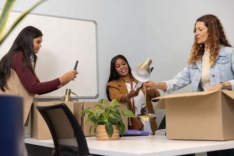 Unpacking boxes and setting up desk lamps — diverse female coworkers collaborating