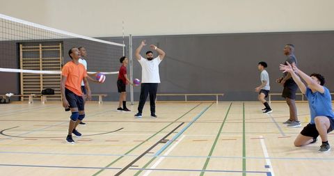 Multiethnic men practicing volleyball in indoor gym showcasing teamwork and coach instruction