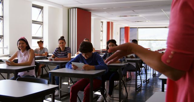 Students sitting at desks while a teacher stands in front creating a dynamic educational atmosphere. Highlights modern classroom environment, can be used for educational materials, school brochures, or articles discussing classroom learning experiences and student engagement.