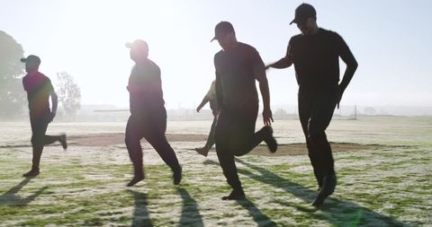 Mature men running at dawn on frost-covered field wearing caps, silhouettes and shadows