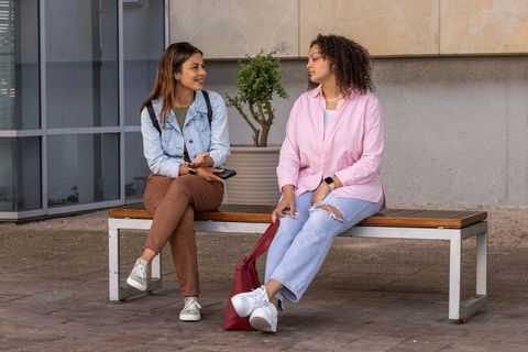 African american women chatting on bench in urban courtyard, casual friends conversing