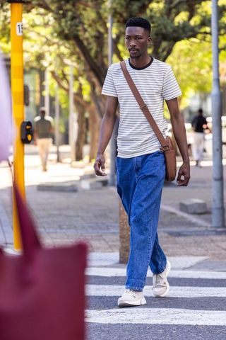 African man walking crosswalk in casual striped tee with satchel urban street lifestyle