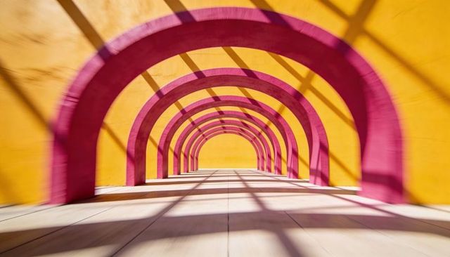 Vibrant magenta arch tunnel with yellow walls and crisscross shadows, strong perspective