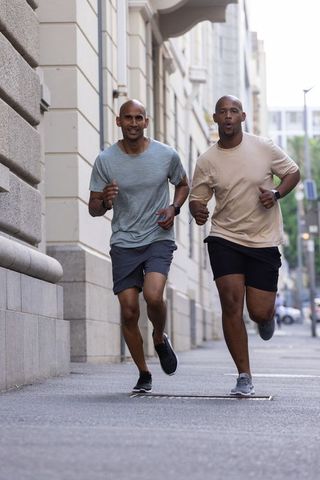 African american friends running together on city sidewalk wearing fitness watches