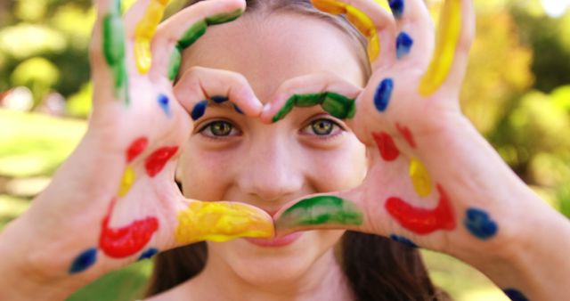 Playful Girl Forming Heart Shape with Colorful Painted Hands Outdoors - Download Free Stock Images Pikwizard.com