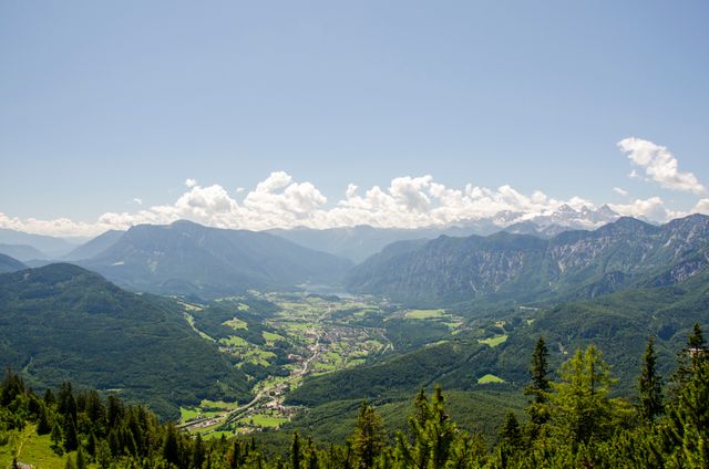 This image captures a stunning vista of a mountainous valley filled with lush forests under a clear blue sky. Ideal for travel blogs, nature-themed websites, brochures about eco-tourism, and posters promoting outdoor activities. Use it to evoke a sense of tranquility, natural beauty, and adventure.