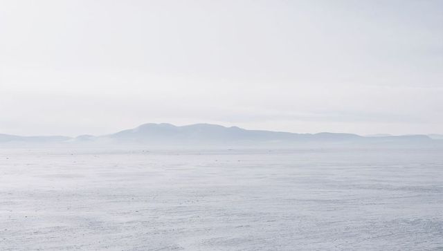 Minimalist misty seascape with distant low hills, calm ripples and panoramic horizon