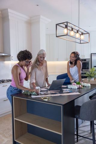 Multi-generational women planning event at modern kitchen island with laptop and flowers
