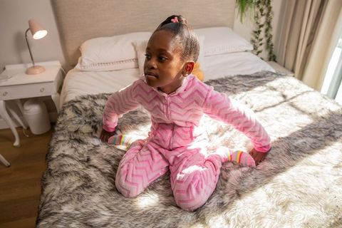 African american girl sitting on bed in pink chevron onesie wearing colorful striped socks