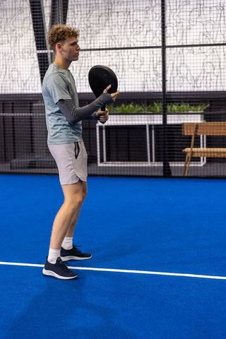 Young male athlete playing padel on indoor blue court holding racket preparing to serve
