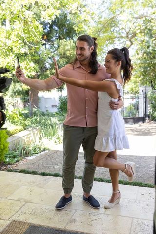 Couple taking selfie on sunlit garden patio embracing while posing for social media
