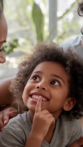 Smiling child touching loose tooth on couch while adults leaning in for family bonding