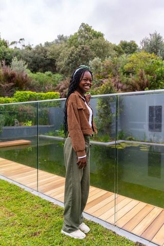 African american woman smiling by glass railing at backyard pond with lush garden greenery