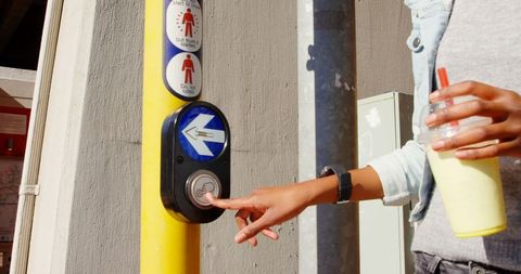 Person pressing street crossing button while holding milkshake