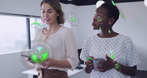 Two women collaborating, tapping tablet and projecting green digital icons in office