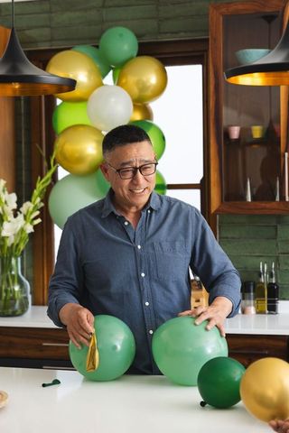 Man arranging green and gold balloons on modern kitchen island for home celebration