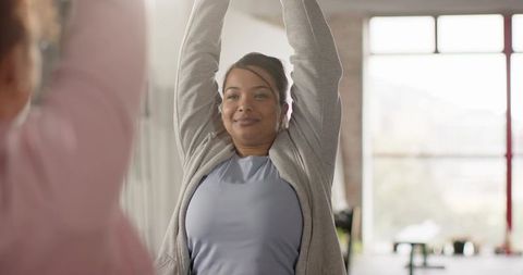 Asian woman stretching during morning workout by bright window wearing light blue top
