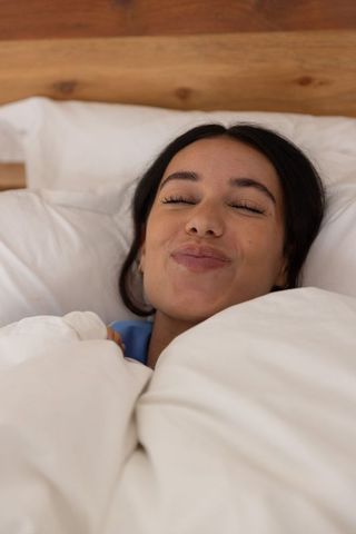 Young woman relaxing in cozy bed wrapped in duvet with serene smile, morning comfort