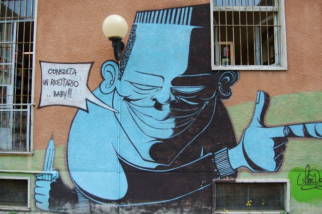 Street art featuring a bold character with a speech bubble on a building wall. Includes a window and a prison-bar design. Artwork adds vibrant culture to the cityscape. Suitable for urban culture, graffiti art, outdoor murals, and city life themes.