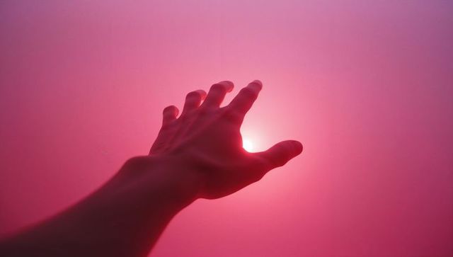 Extended hand reaching for radiant light through gradient pink red haze
