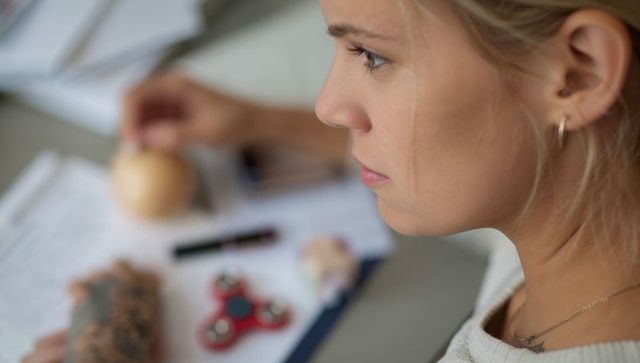 Young woman concentrating on documents at desk with fidget spinner and clipboard
