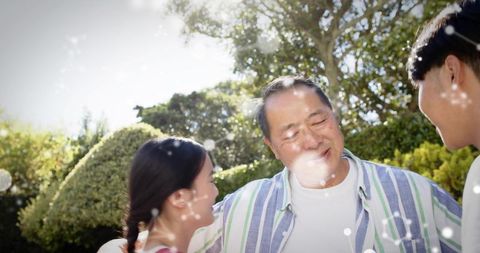 Smiling senior man hugging daughter and son in sunlit garden, family warmth and affection