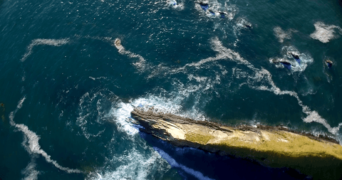Transparent Blue Ocean Aerial View with Waves Crashing on Rocks