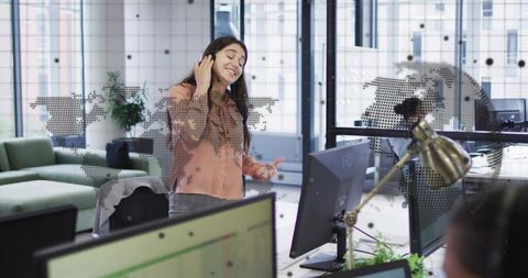 Young professional enjoying music with headphones in modern open-plan office with glass partition