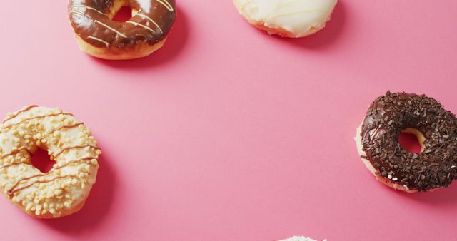 Assorted variety of donuts with different toppings such as sprinkles, glaze, and frosting, arranged on a vibrant pink background. Perfect for use in food blogs, bakery advertisements, social media posts about sweets, and promotional materials for dessert shops.